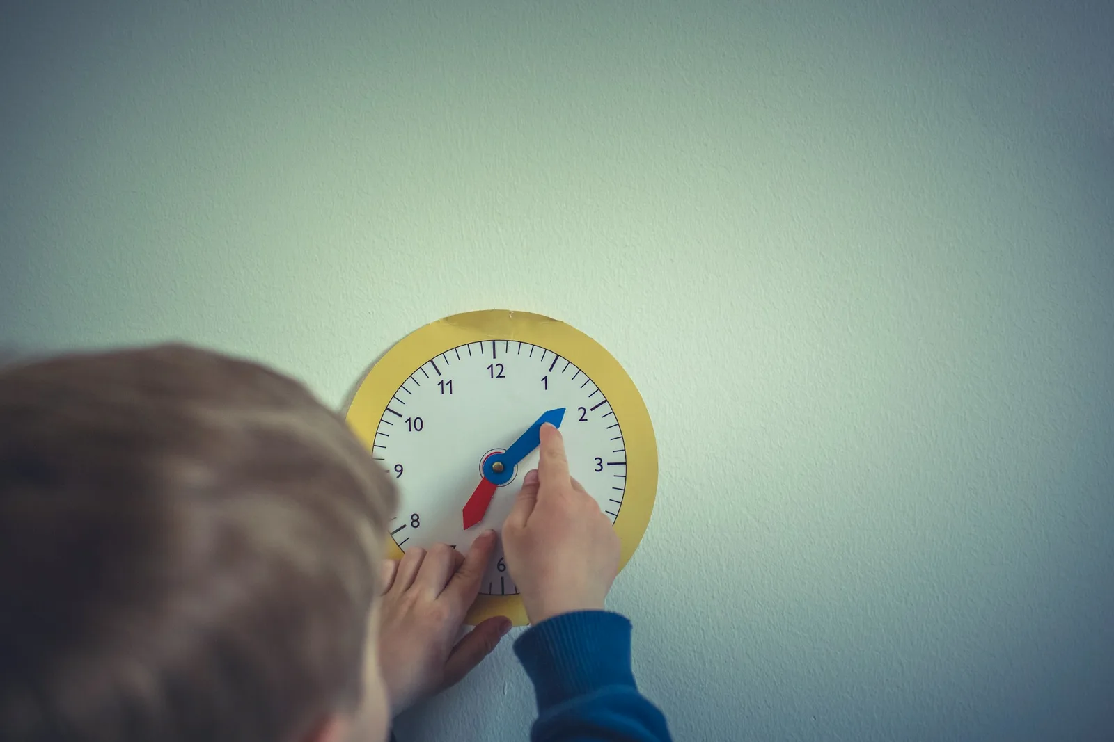 Child adjusting the hands of a yellow toy clock fixed to the wall
