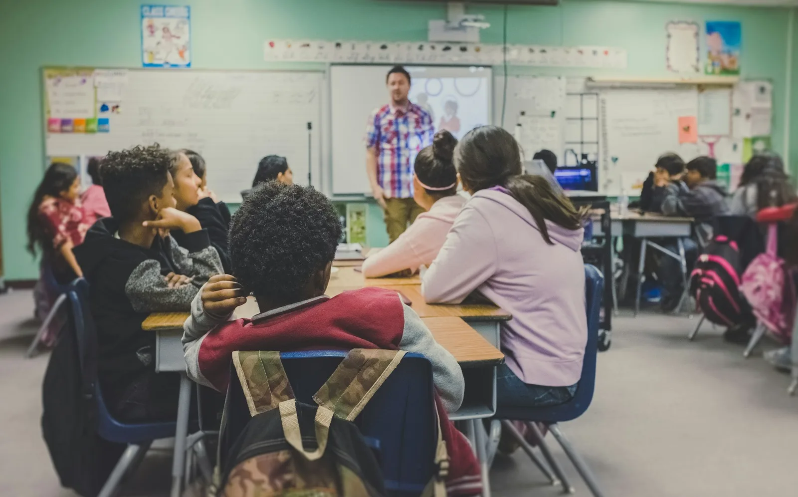 Students seated in a classroom watching the teacher at the front by the board