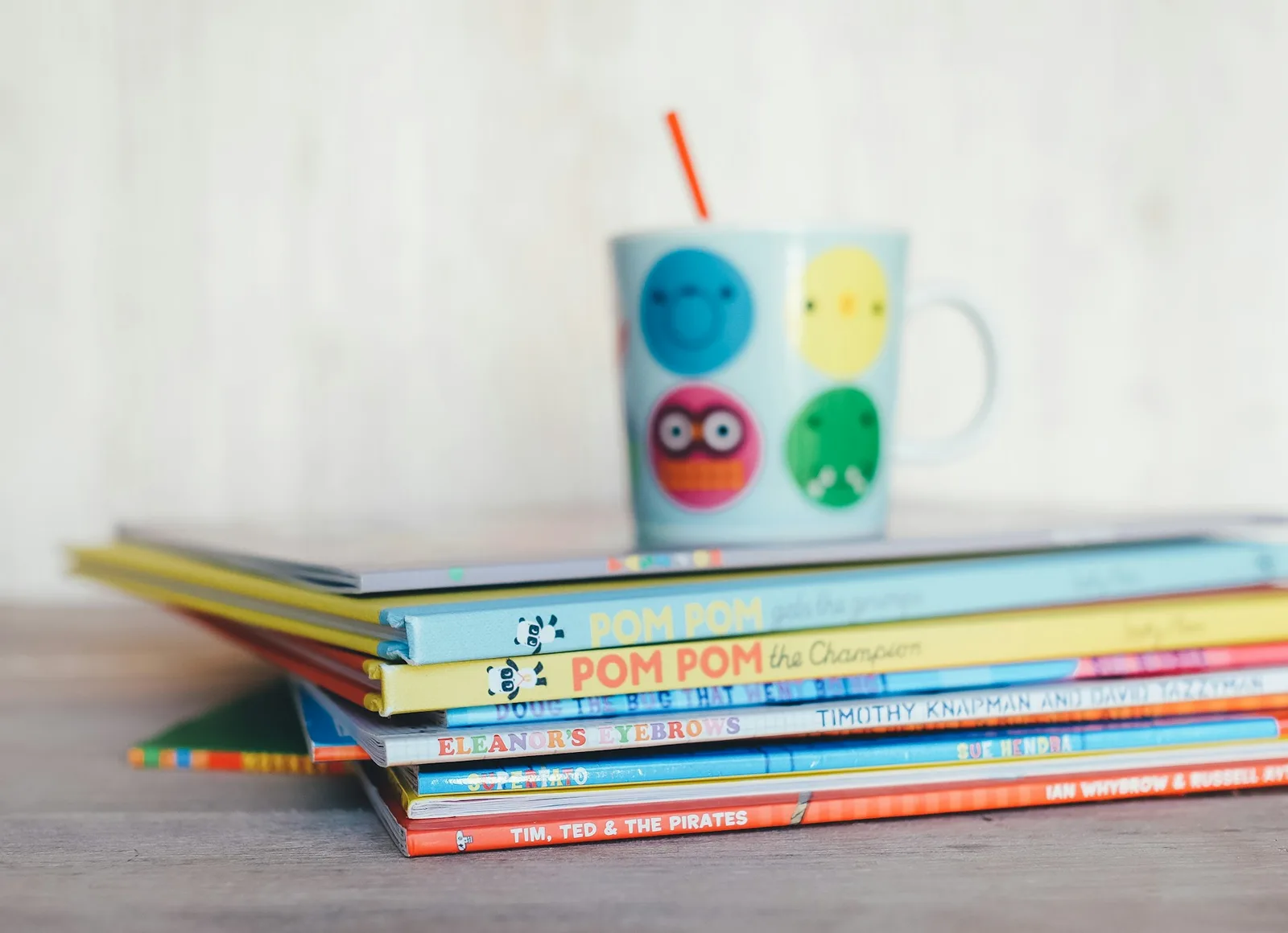 Stack of colorful children's books with a patterned mug on top