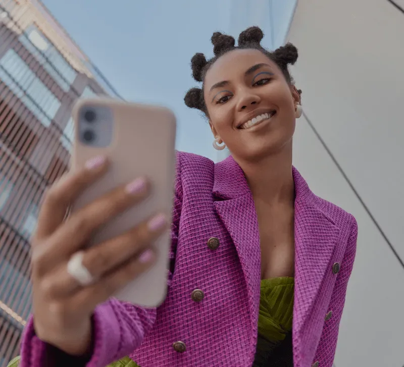 Smiling woman in a purple blazer holding her phone in front of her, with buildings behind