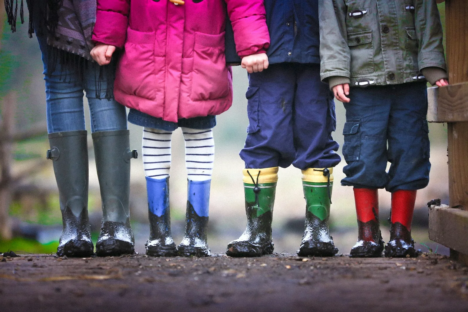 Cuatro niños con abrigo y botas de goma en fila por un camino de tierra