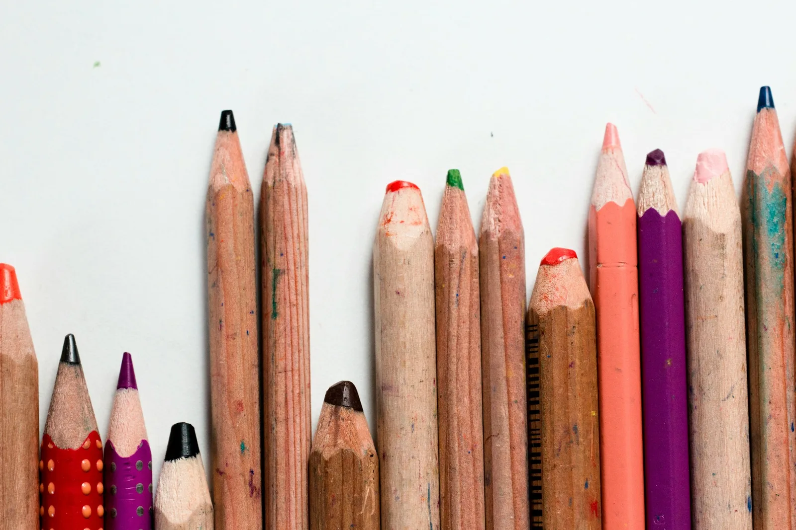 Fila de lápices de color usados, cada uno con una altura diferente, sobre fondo blanco