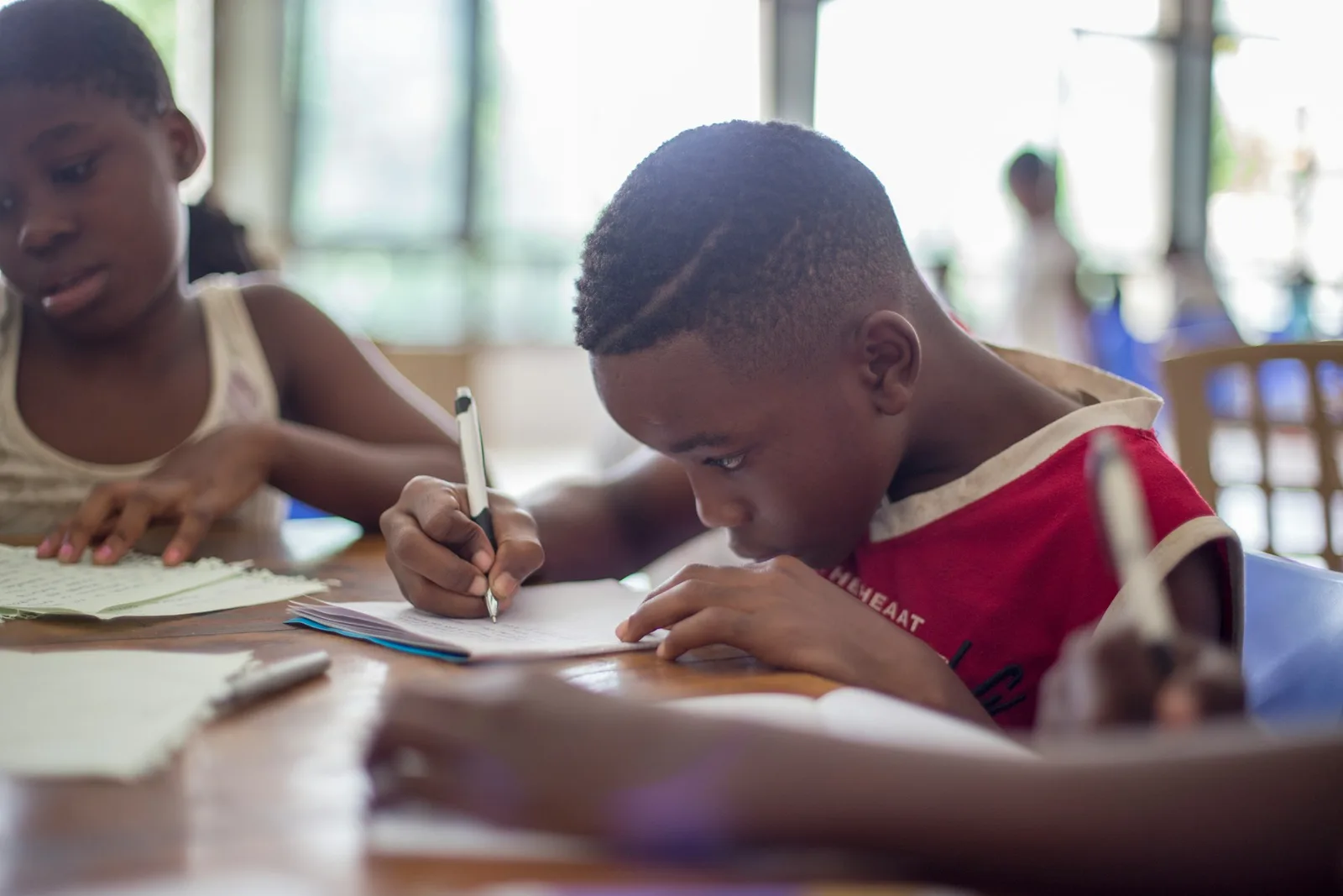 Two students writing in notebooks while seated at a wooden table