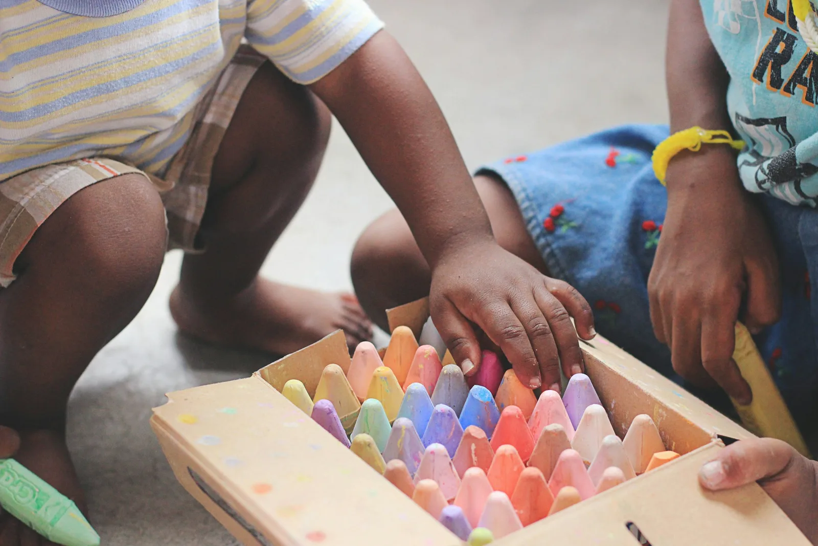 Dos niños agachados en el suelo eligen tizas de colores en una caja de cartón